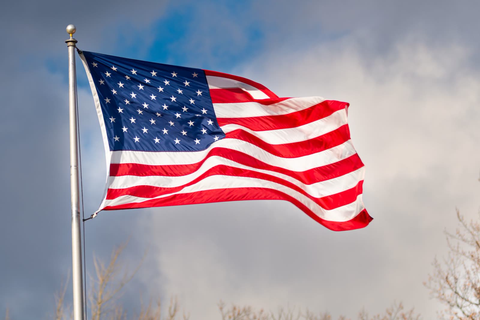people walking a downtown sidewalk under windy gray autumn skies / flag snapping in the wind on a warm cloudy fall afternoon / storm clouds building over a small Southern town skyline