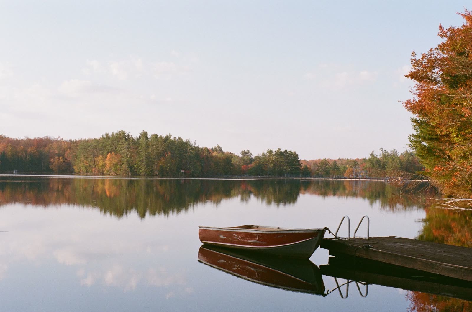 anglers in a small boat on calm lake water at sunrise in autumn / people sitting on a wooden lake dock on a cool fall morning / quiet reservoir with fall color along the shoreline