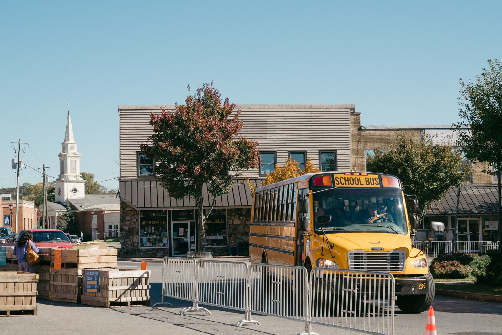 children in hoodies with backpacks waiting at a school bus stop on a cool fall m / kids standing on a neighborhood corner in the early morning in autumn / yellow school bus on a small town street under fall trees